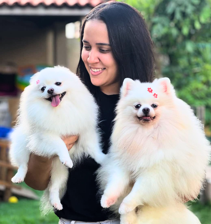 Juliana sorrindo, com dois Pomeranians brancos no colo